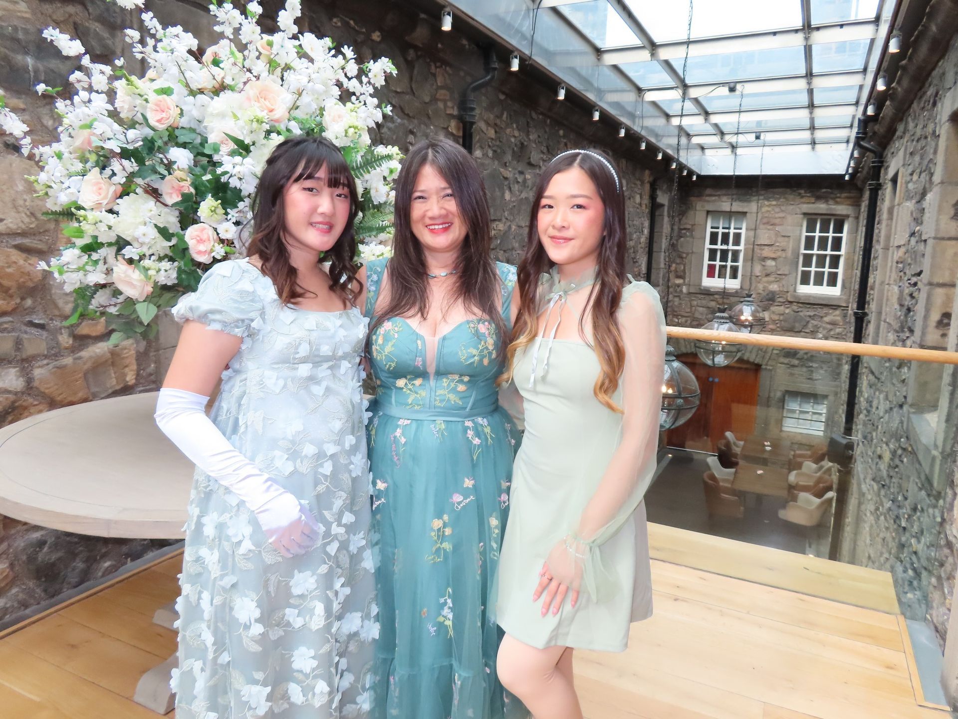 Three women are posing for a picture in front of a vase of flowers.