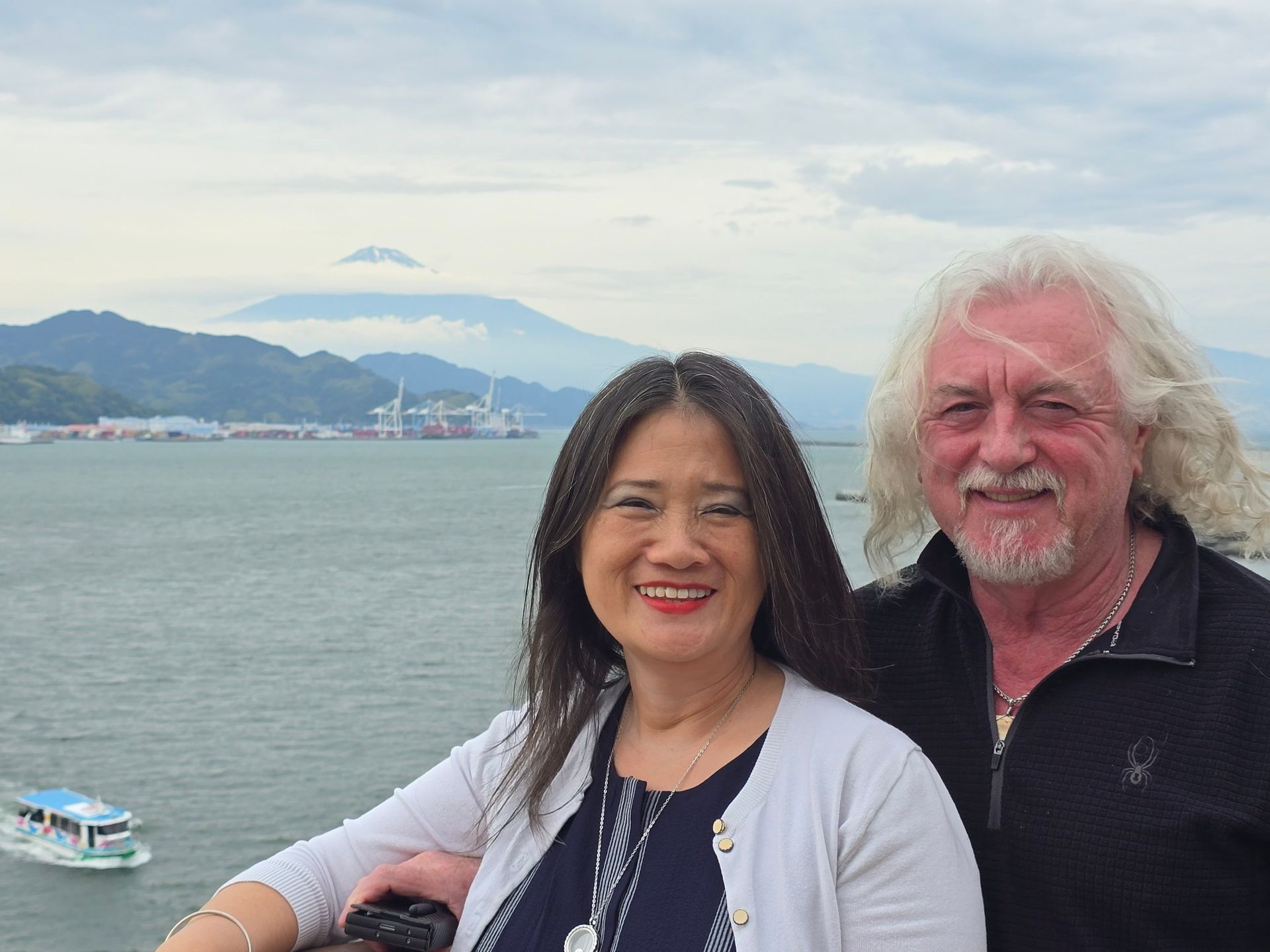 A man and a woman are posing for a picture in front of a body of water.