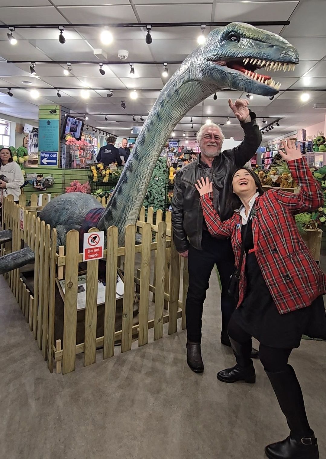 A man and a woman are posing in front of a dinosaur statue.