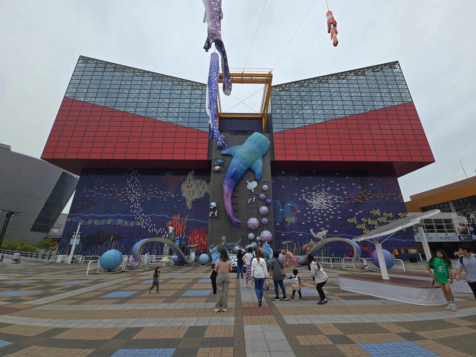 A group of people are standing in front of a large building with a dolphin hanging from it.