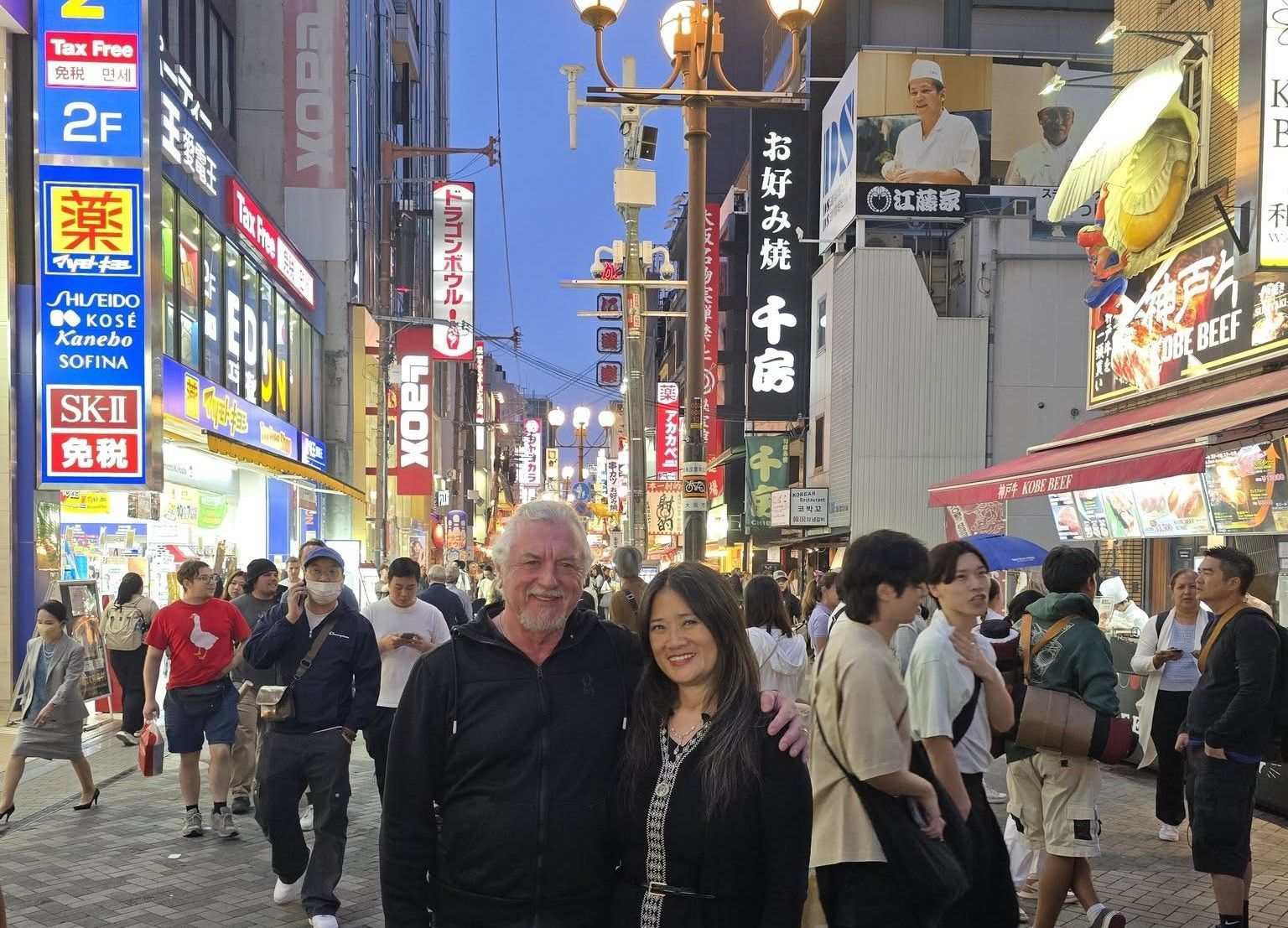 A man and a woman are posing for a picture on a busy street