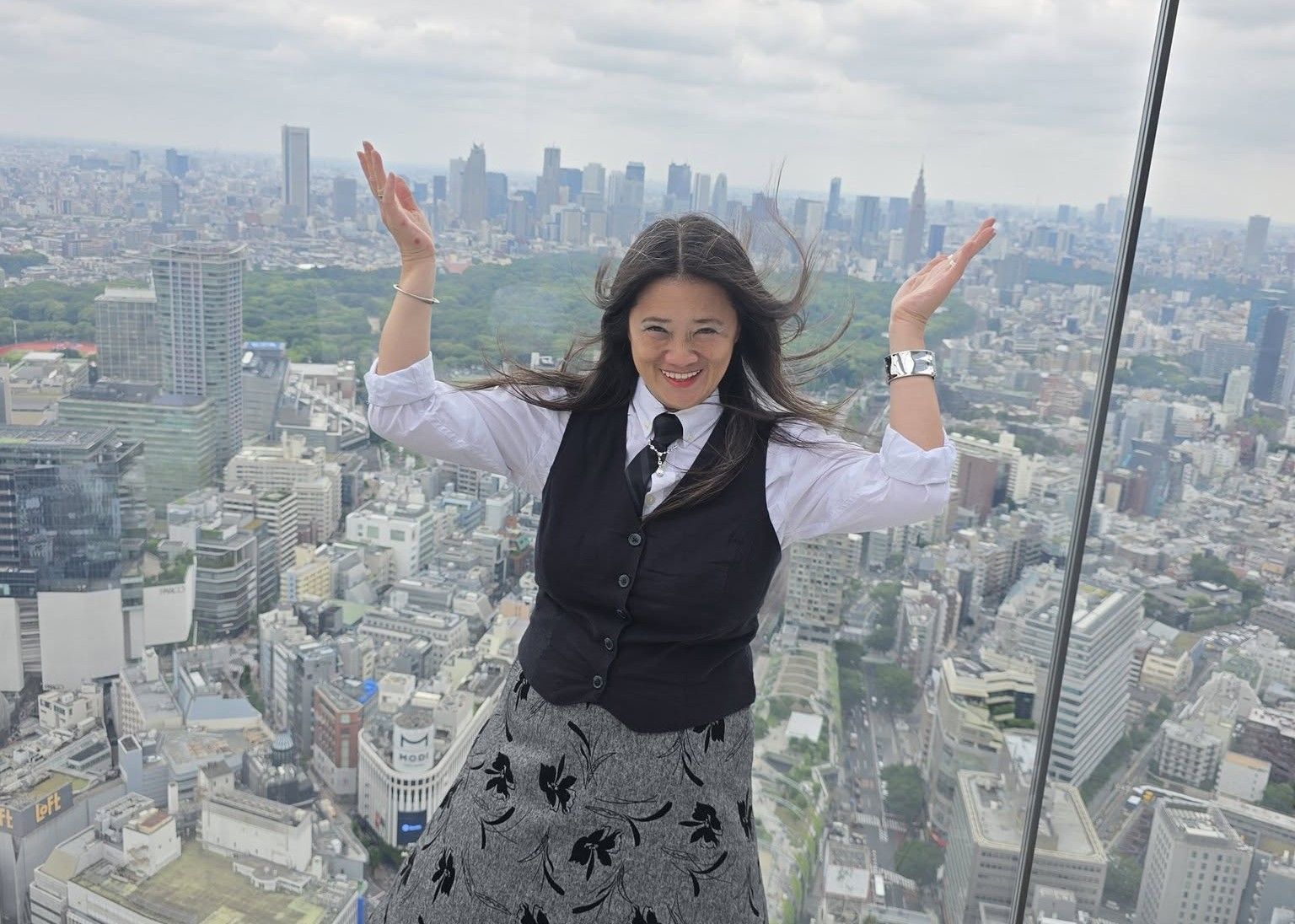 A woman is standing in front of a city skyline with her arms in the air.