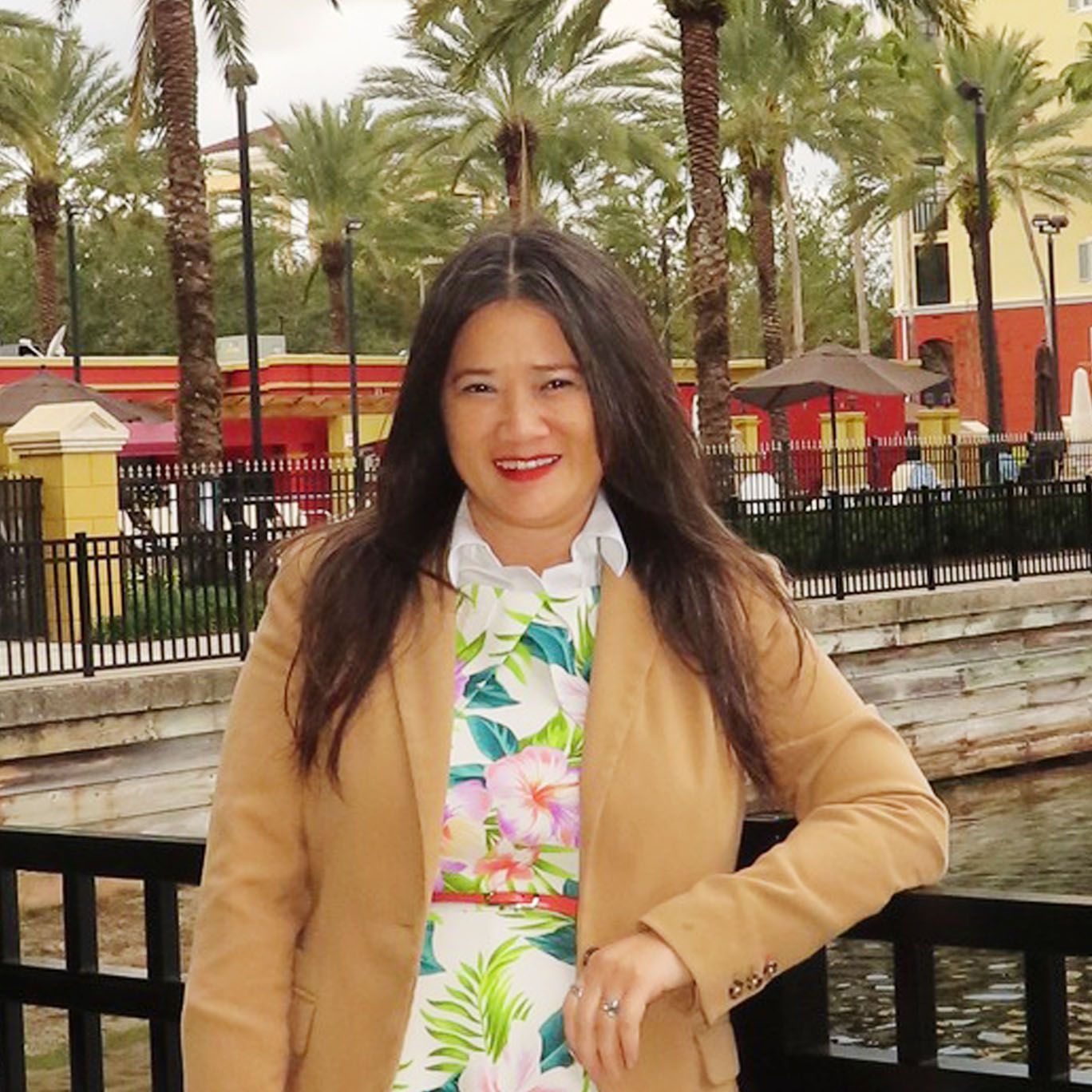A woman wearing a tan jacket and a floral shirt smiles for the camera