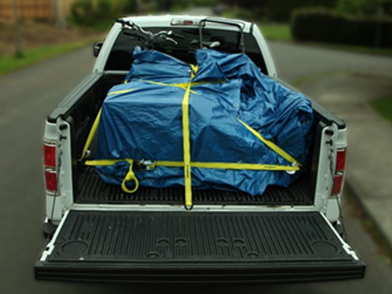 A pickup truck is loaded with a blue tarp and yellow straps