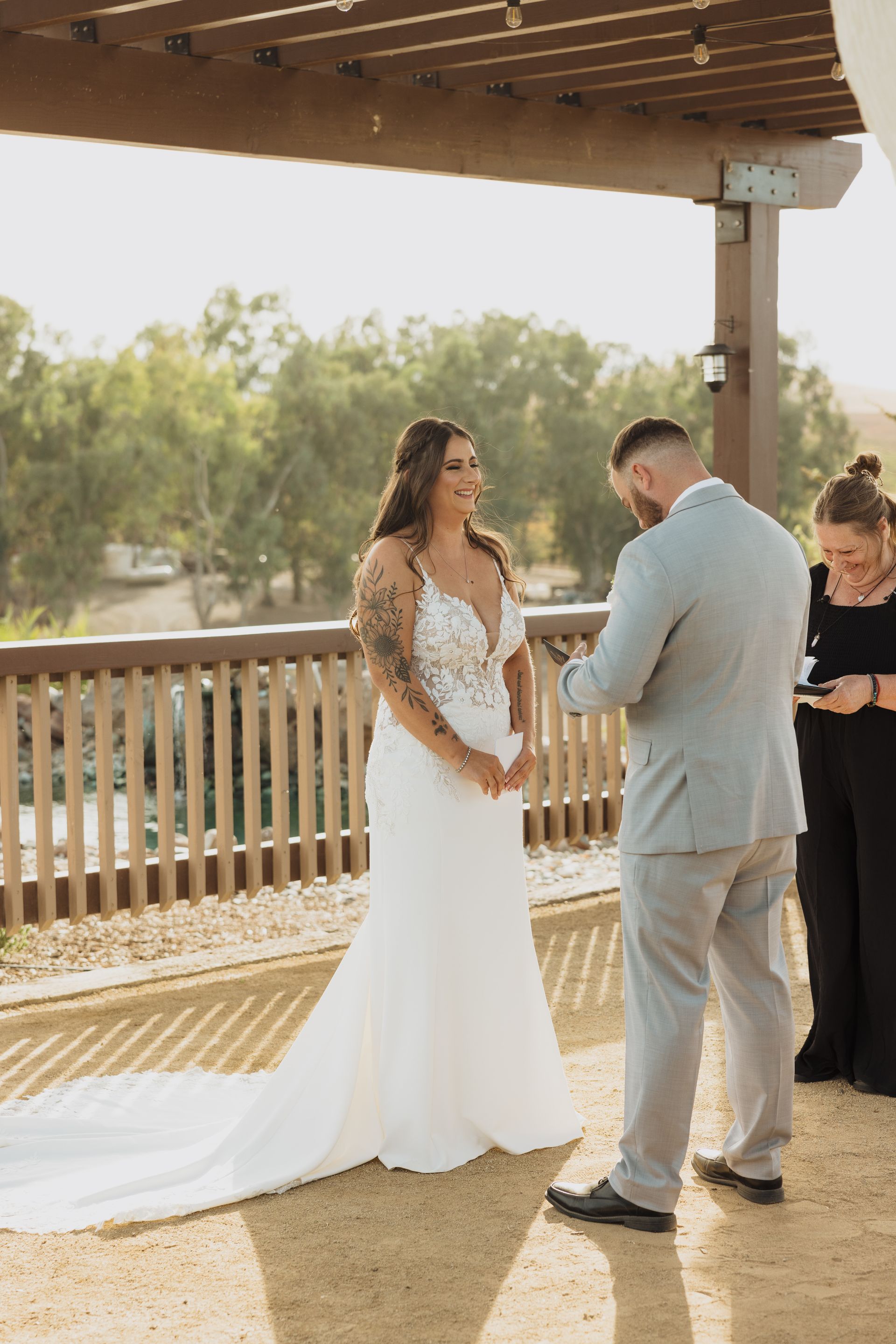 A bride and groom are walking through a vineyard holding hands.