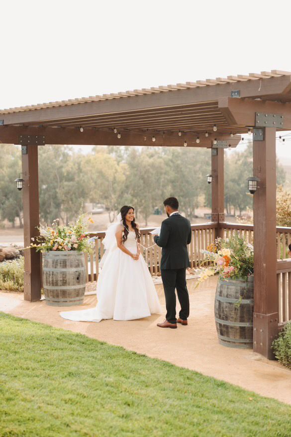 A bride and groom are standing under a pergola.