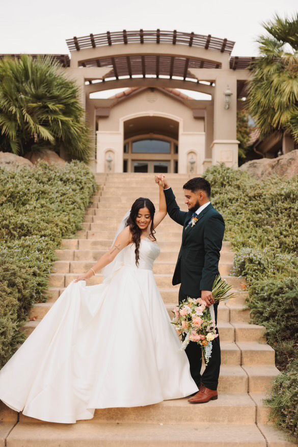 A bride and groom are standing on a set of stairs holding hands.