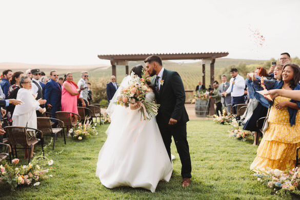 A bride and groom are kissing while walking down the aisle at their wedding.
