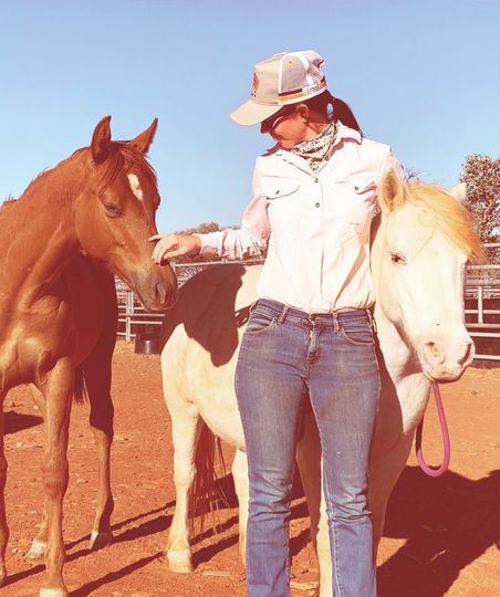 An animal nutritionist is standing next to two horses one brown and one white