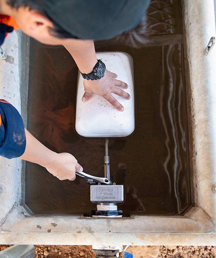 A person is cleaning float system in a water trough with a wrench