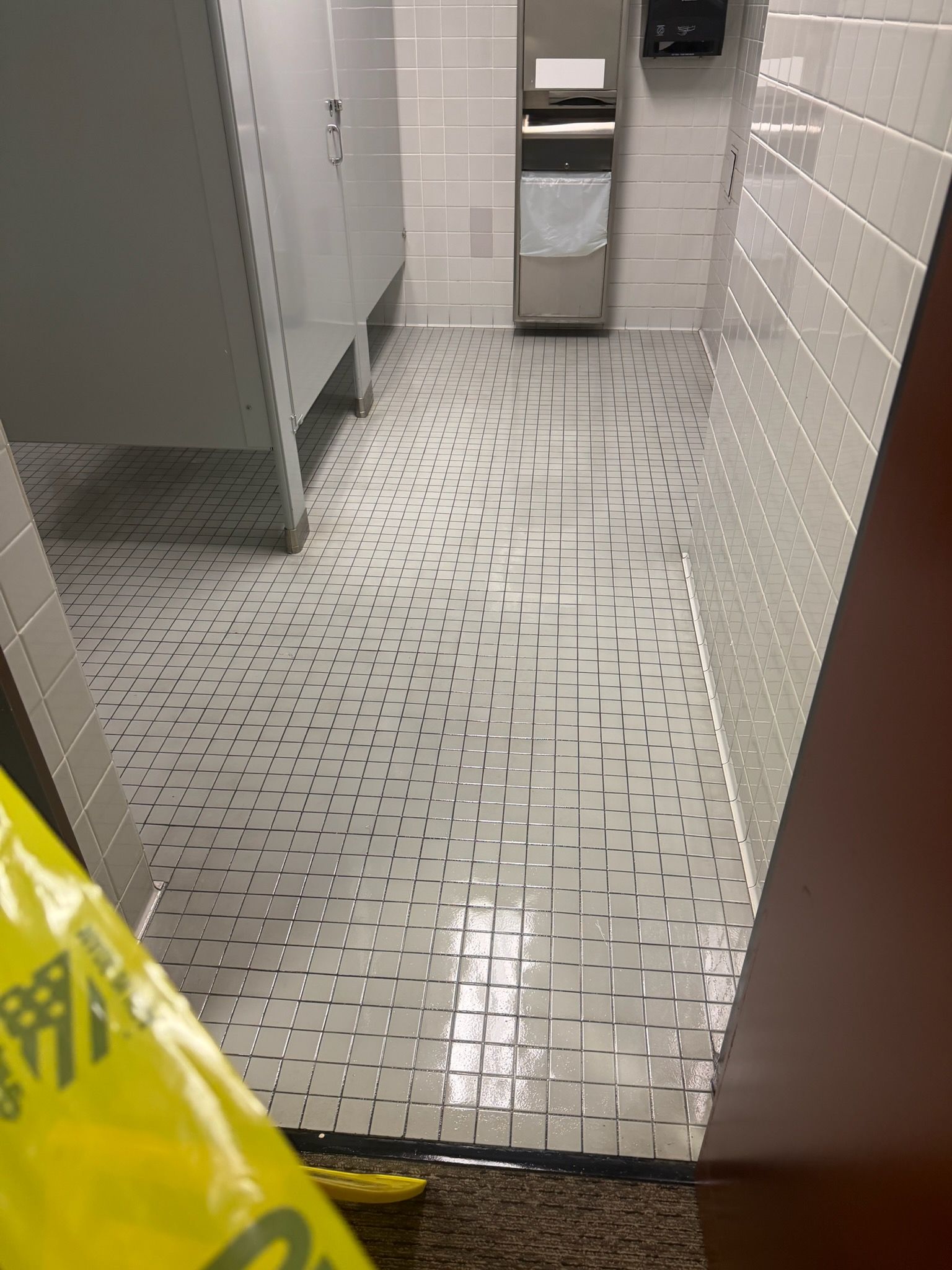 Restroom floor with pooled water and caution tape near stalls and a trash can