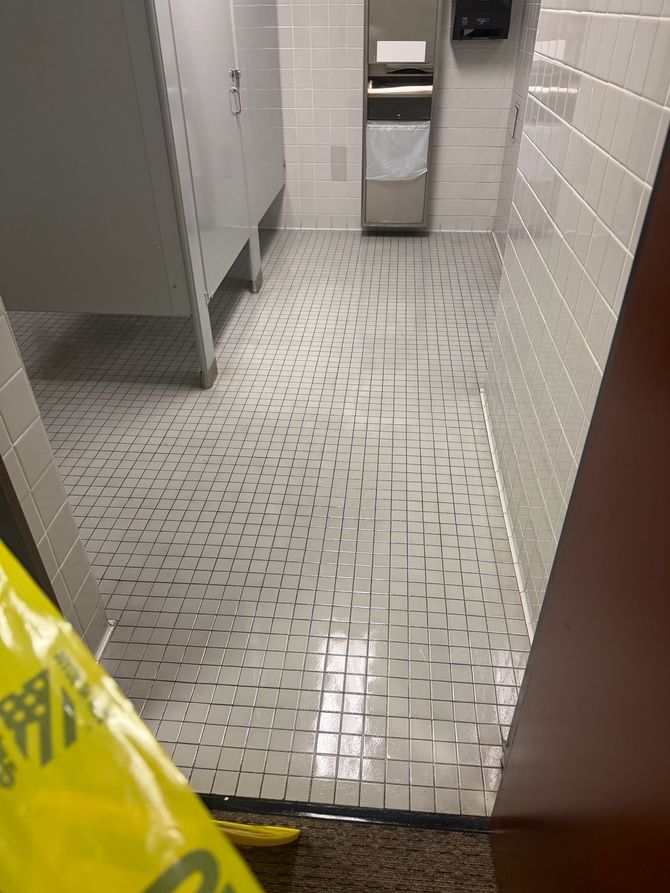 Restroom floor with pooled water and caution tape near stalls and a trash can