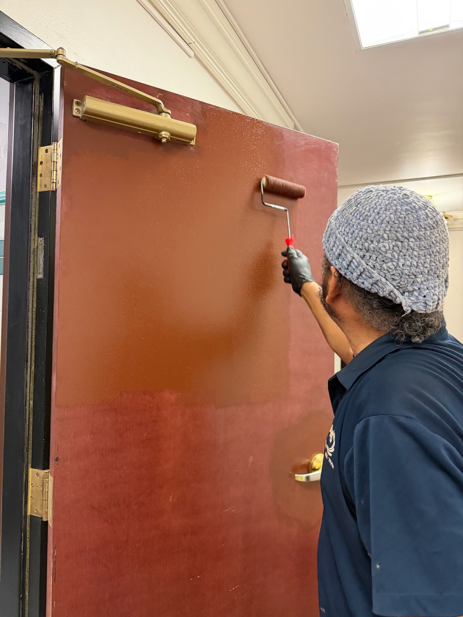 Person painting a red door with a roller in an indoor hallway