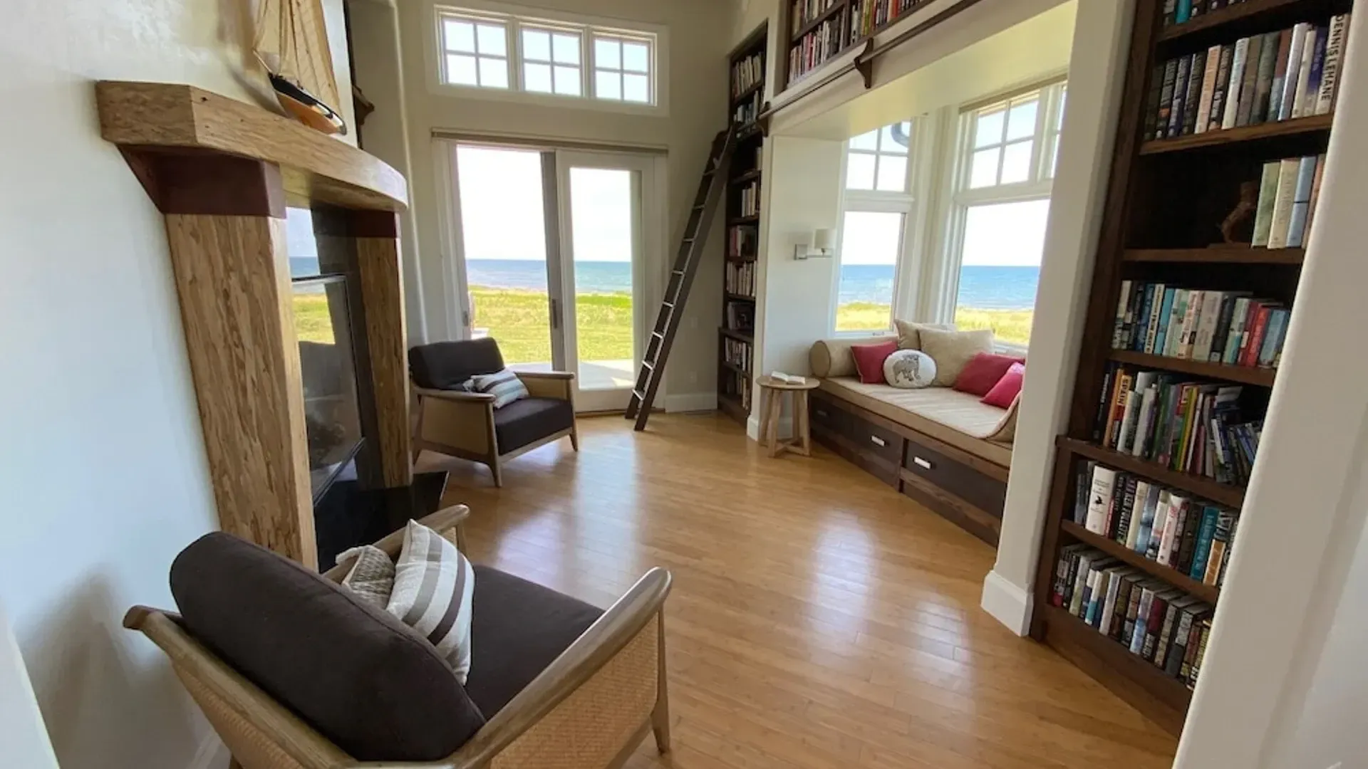 Gezellige woonkamer met houten vloer, boekenkast, fauteuils, erker en een ladder met een prachtig uitzicht.