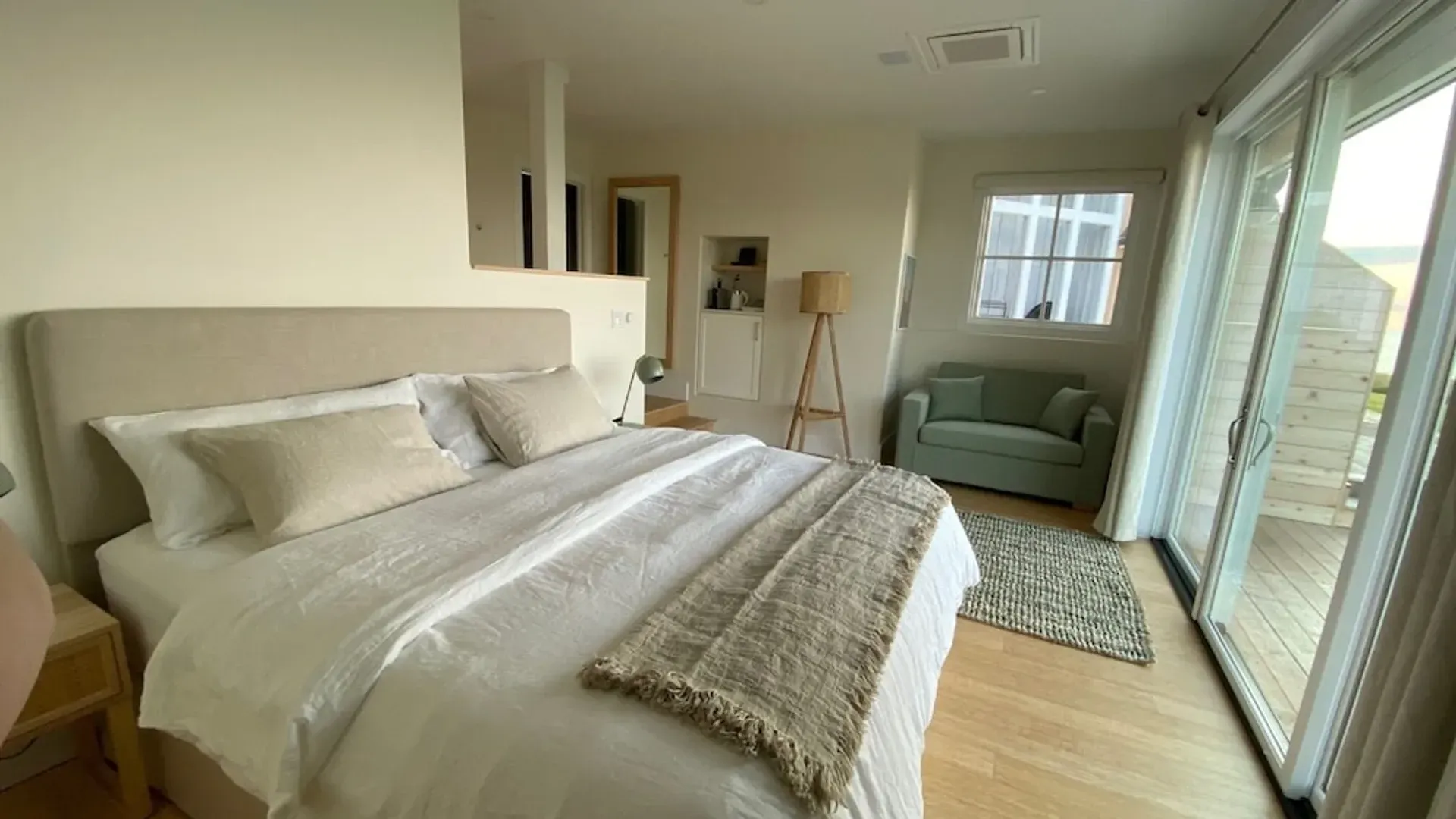 Lichte slaapkamer met een netjes opgemaakt bed, lichte houten vloeren en een zithoek bij het raam.