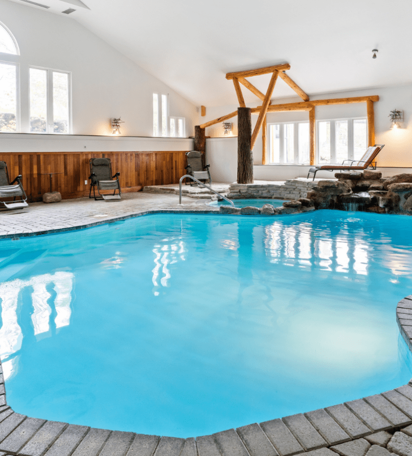 Binnenzwembad met turquoise water, houten lambrisering, ligstoelen en een stenen terras.