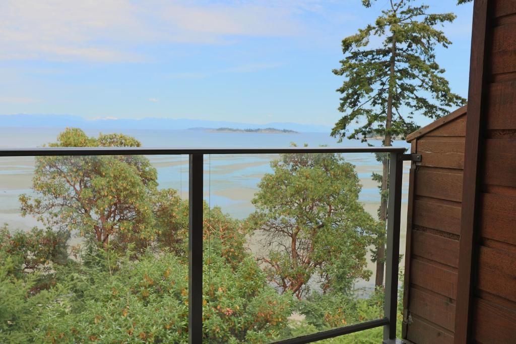 Uitzicht vanaf het balkon op een kalm blauw meer met bomen en een metalen reling op de voorgrond.
