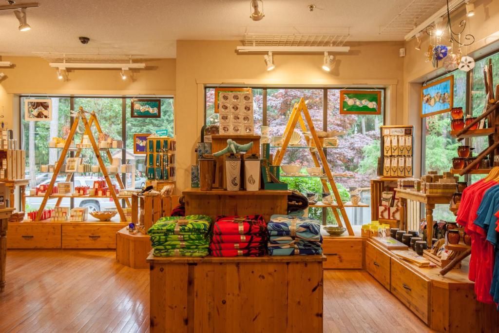 Licht en sfeervol boetiekinterieur met houten vitrines, kleurrijke opgevouwen kleding en grote ramen die daglicht binnenlaten.