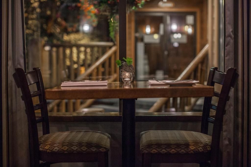 Gezellige restauranttafel bij het raam, met houten stoelen en warme avondverlichting op de achtergrond.