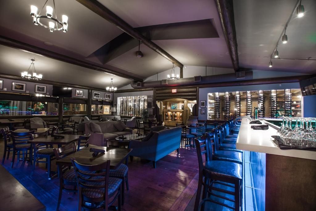 Een moderne bar met gedimd licht, blauw gestoffeerde stoelen, tafels, planken en een lange toonbank met flessen en glazen.