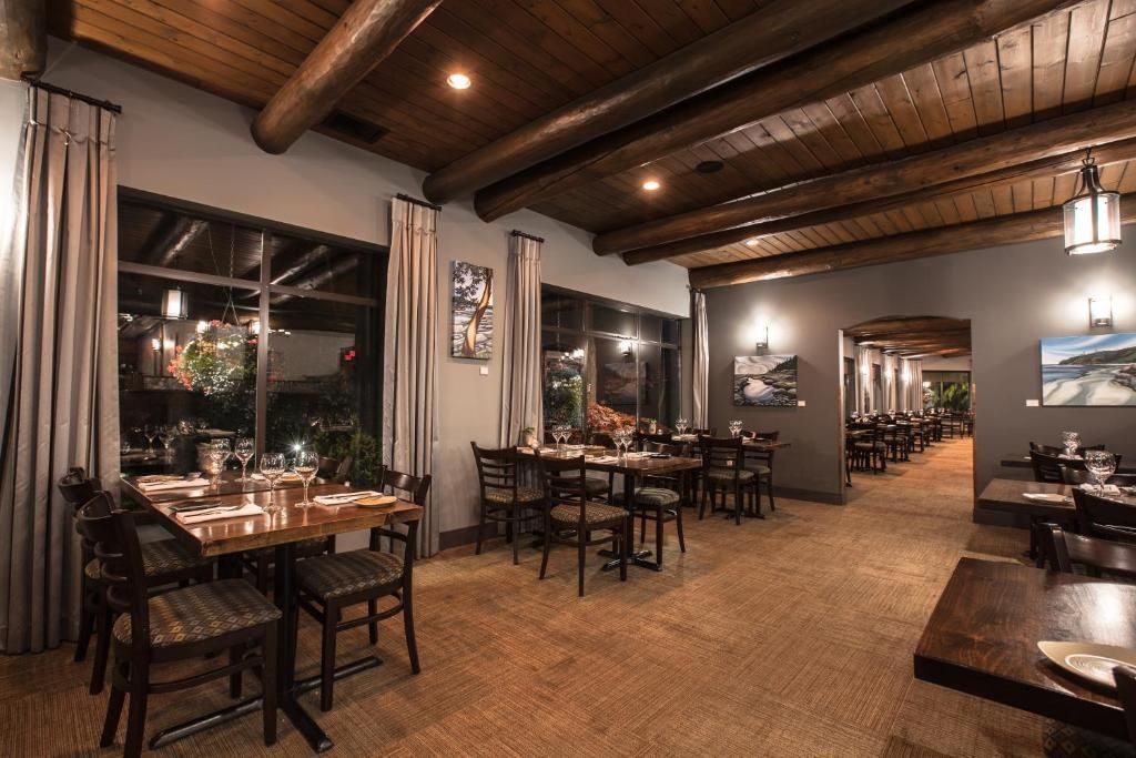 Elegante restaurantzaal met houten tafels, warme verlichting en een plafond met zichtbare balken.