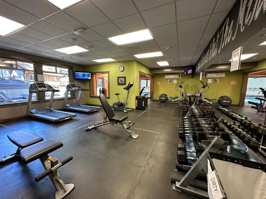 Een lege sportschool met loopbanden, dumbbells en gewichtbanken onder fel tl-licht.
