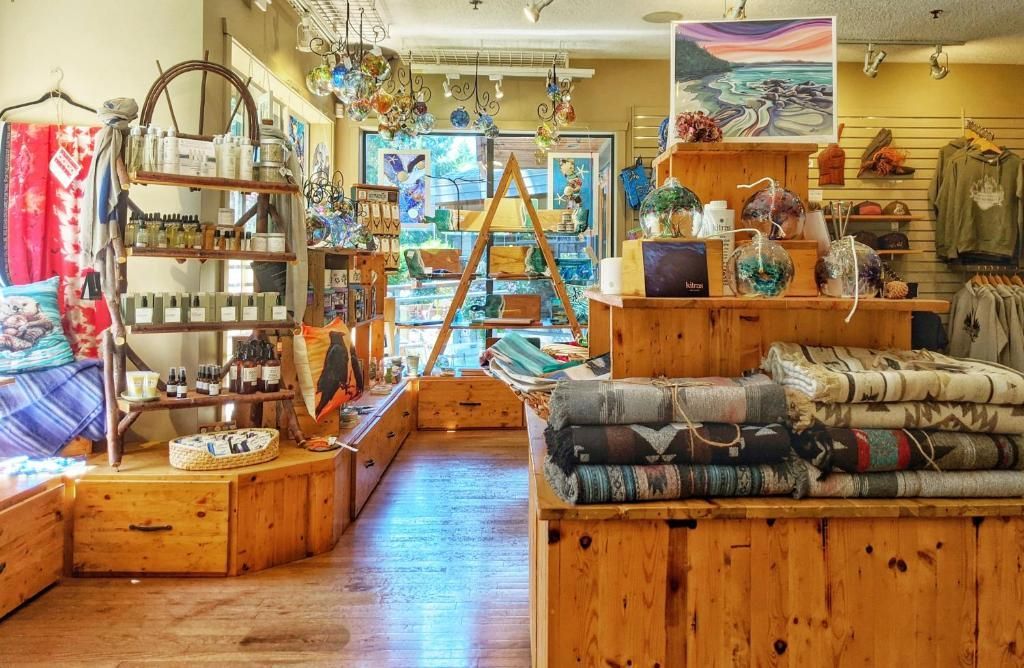 Gezellig, rustiek winkelinterieur met houten vitrines, opgevouwen dekens, planken en kleurrijke kunst aan de muren.