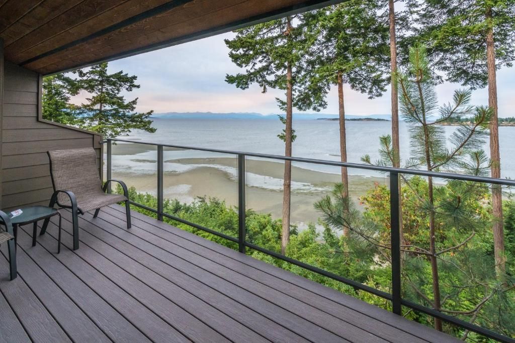 Overdekt terras met uitzicht op een kalme oceaan, met glazen balustrade en een stoel aan de linkerkant.