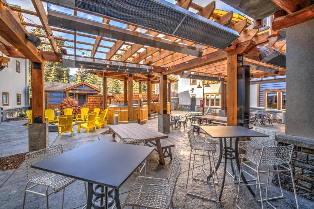 Terras van een café in de buitenlucht met metalen tafels en stoelen onder een houten pergola, warm zonlicht en een stenen vloer.