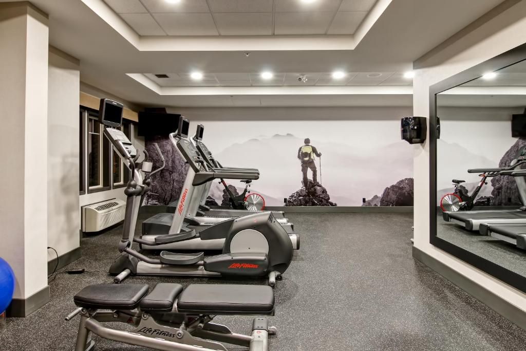 Fitnessruimte met loopbanden, een spiegel aan de muur en hometrainers in een trainingsruimte met vloerbedekking.