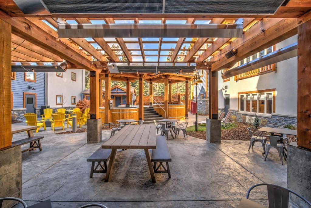 Overdekte buitenpatio met houten pergola, picknicktafels, banken en sfeervolle avondverlichting.