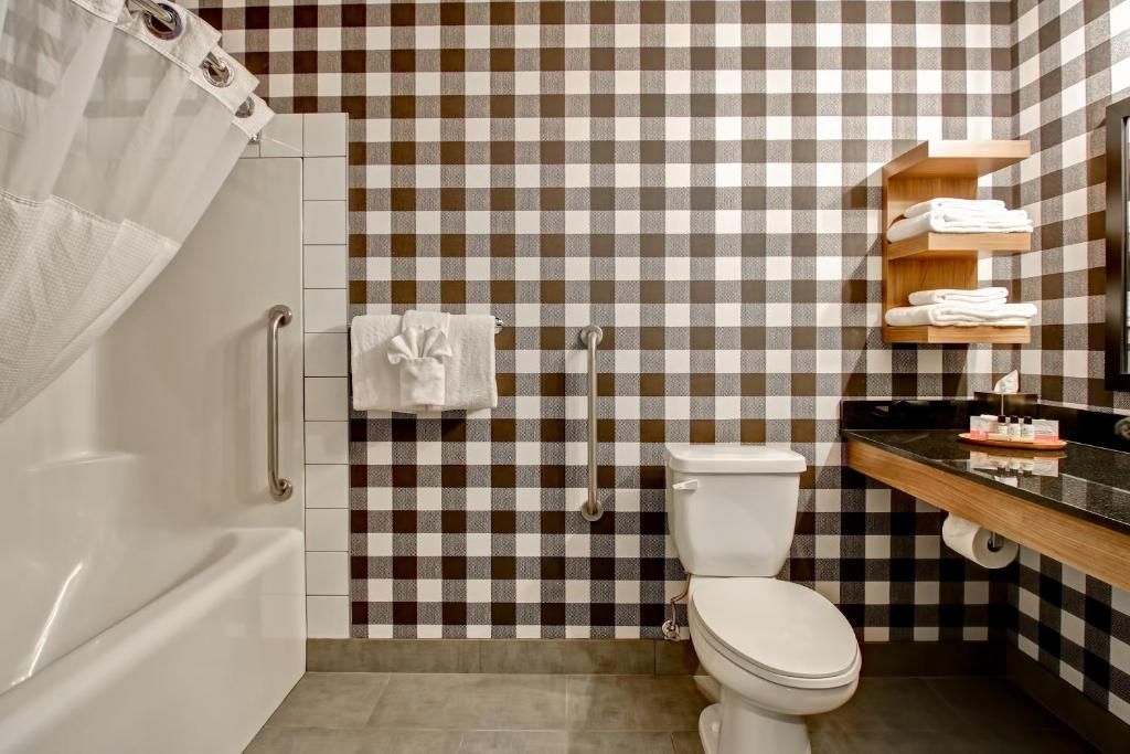 Kleine badkamer met geblokt bruin-wit behang, toilet, badkuip en wastafel op het aanrecht.