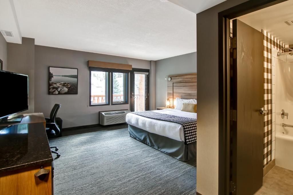 Kleine hotelkamer met bed, bureau, stoel, raam en een deur naar de badkamer.