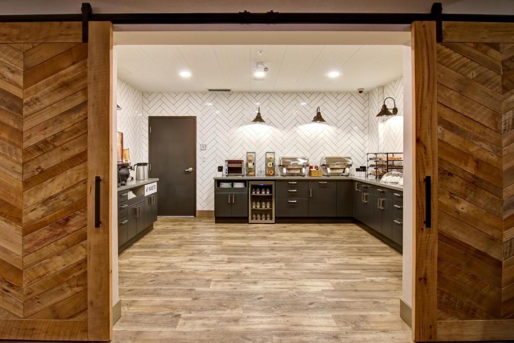 Openslaande houten deuren onthullen een moderne keuken met donkere kasten, houten vloeren en inbouwverlichting.
