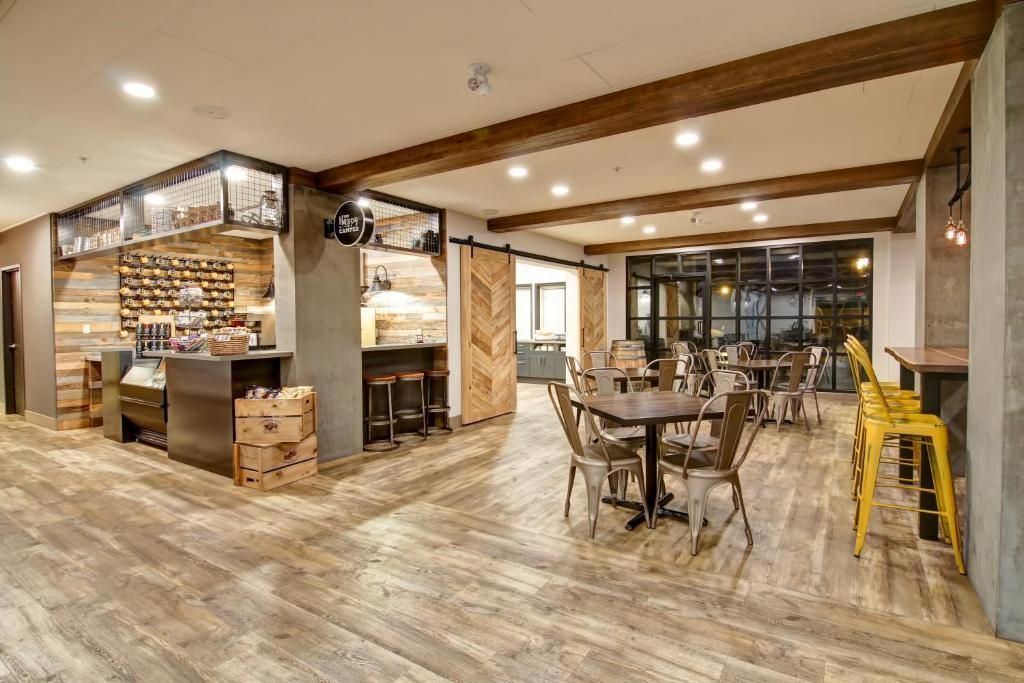 Modern café-interieur met houten tafels, stoelen, een bar en warme sfeerverlichting.
