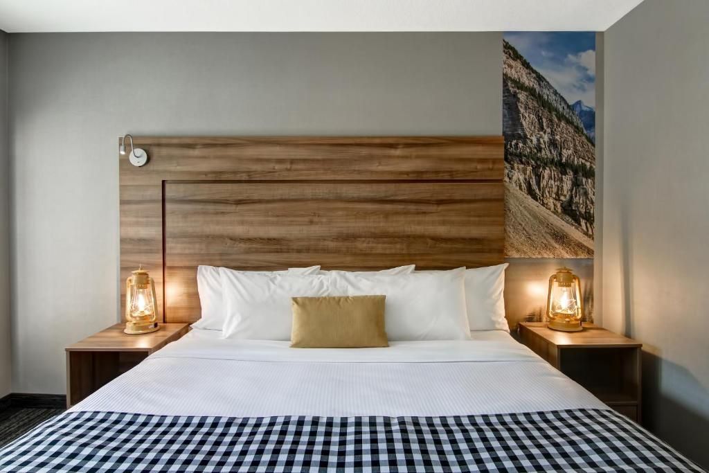 Moderne hotelkamer met een houten hoofdeinde, wit beddengoed en nachtlampjes.