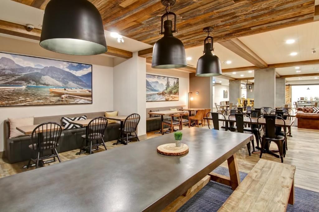 Moderne restaurantzaal met lange tafel, hangende pendellampen en wanddecoratie.