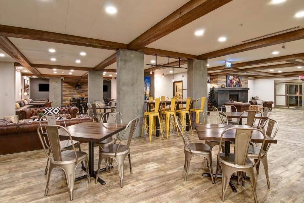 Een lege eetruimte in een restaurant met houten tafels, metalen stoelen en gele barkrukken onder inbouwverlichting.