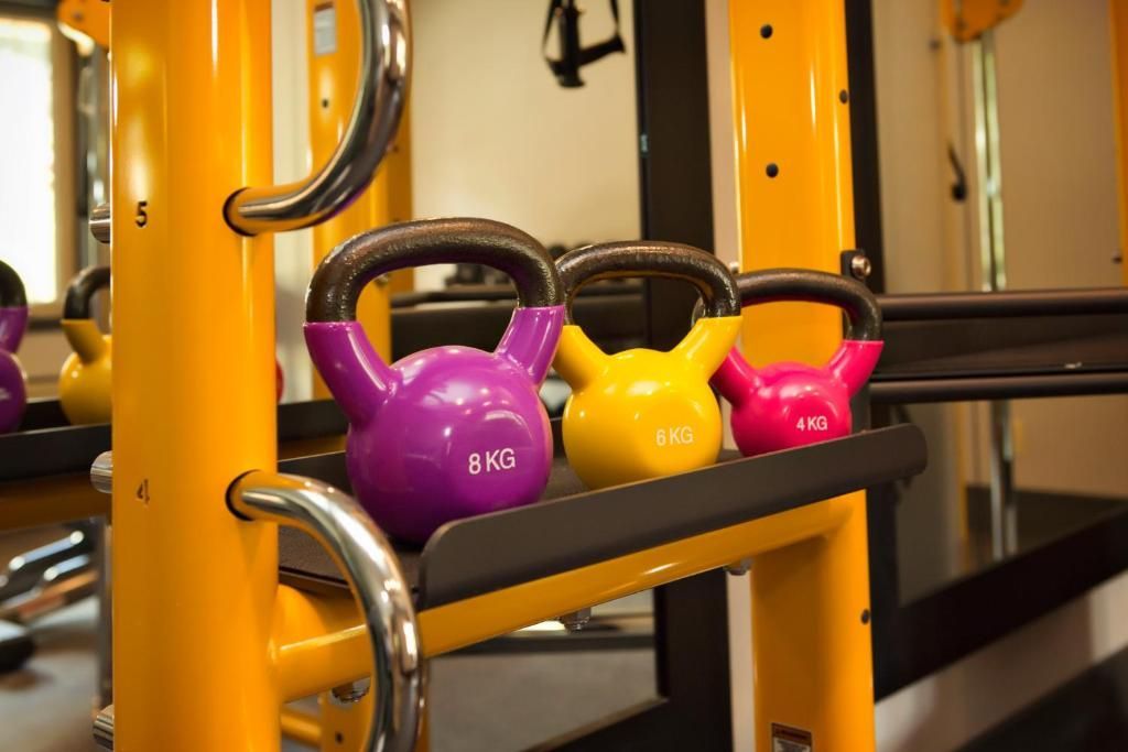 Drie kettlebells in paars, geel en roze op een fitnessrek.