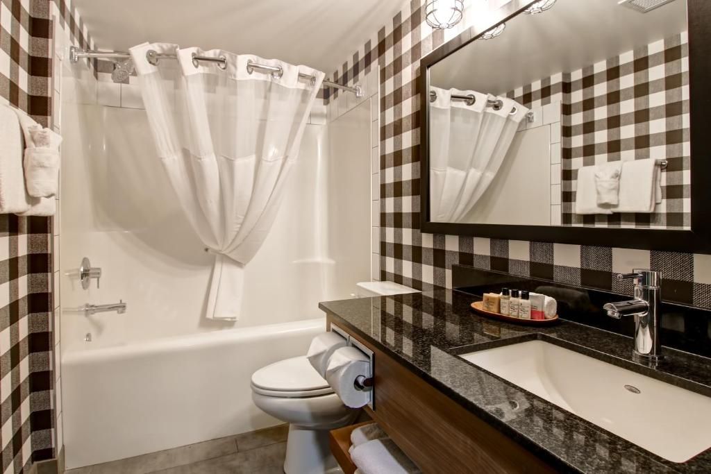 Kleine badkamer met bad, toilet en wastafel, met bruin-wit geblokte muren en een grote spiegel.