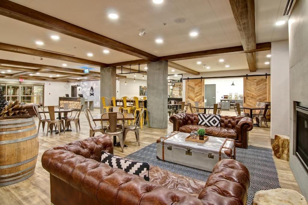 Rustieke lounge met leren banken, tafels van vaten en warme houten balken in een ruime binnenruimte.