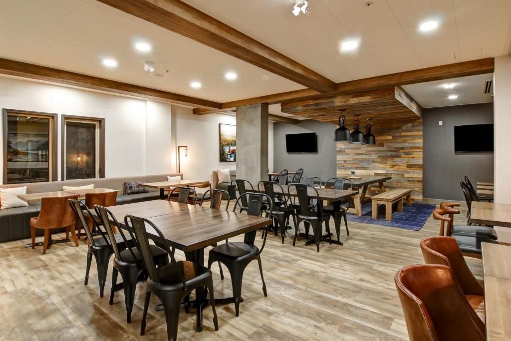 Ruime, moderne eetzaal met verspreide tafels, zwarte stoelen, houten balken en accentmuren van natuursteen.