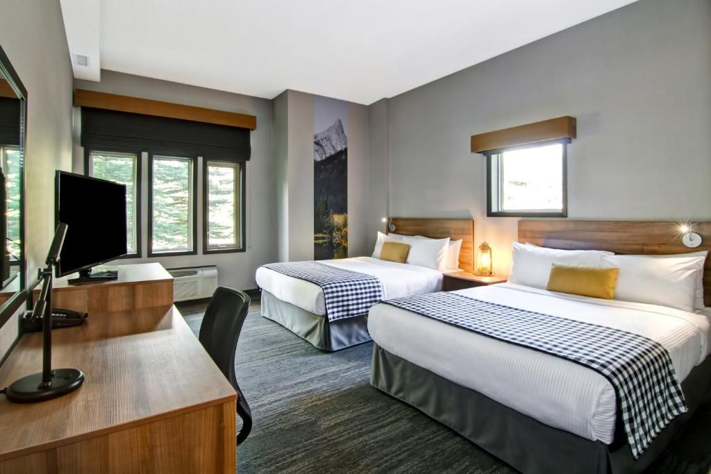 Hotelkamer met twee bedden, tv en grote ramen, ingericht in grijze en blauwe tinten.