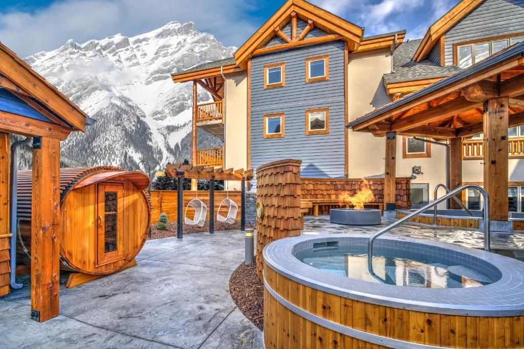 Binnenplaats van een resort in de besneeuwde bergen met houten huisjes en een ronde buitenjacuzzi.