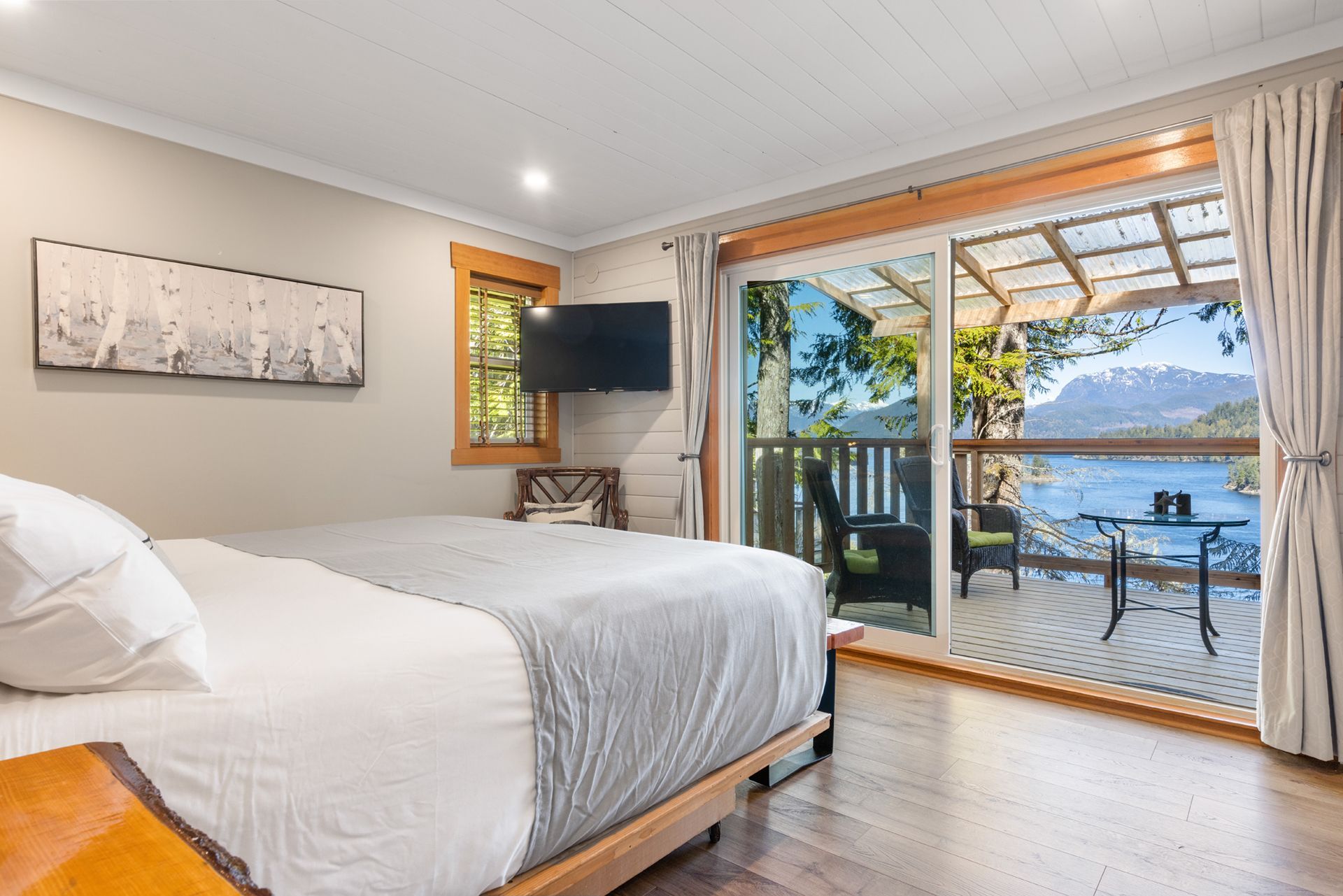Lichte slaapkamer met een groot bed en schuifdeuren die toegang geven tot een terras aan het meer met uitzicht op het water.