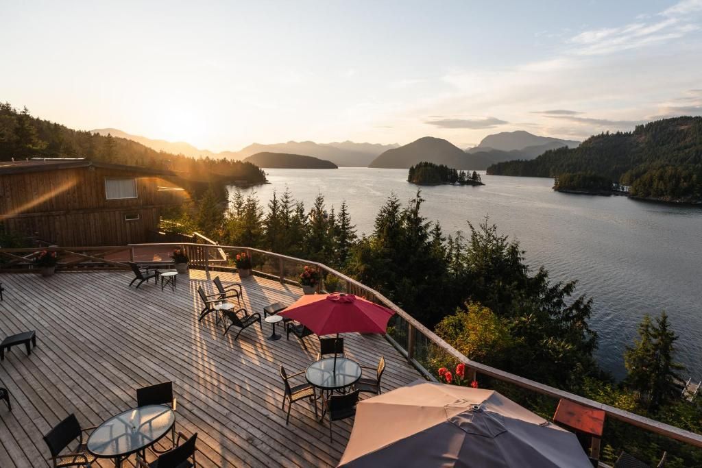 Zonnig terras aan het meer met tafels, parasols en uitzicht op de bergen bij zonsondergang.