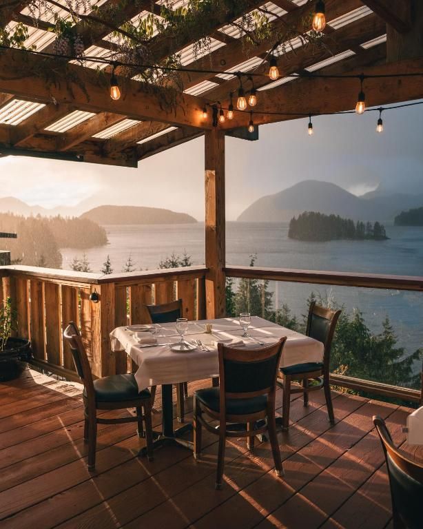 Overdekt terras aan het meer om bij zonsondergang te dineren, met tafels, sfeerverlichting en uitzicht op de bergen.