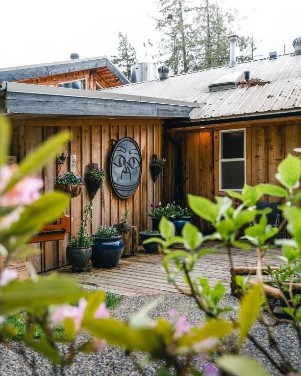 Terras bij een houten blokhut met potplanten, ovale muurdecoratie en groen ervoor.