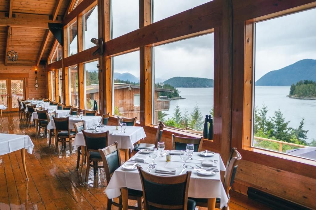 Rustiek restaurant aan het meer met witte tafelkleden en grote ramen met uitzicht op de bergen en het water.