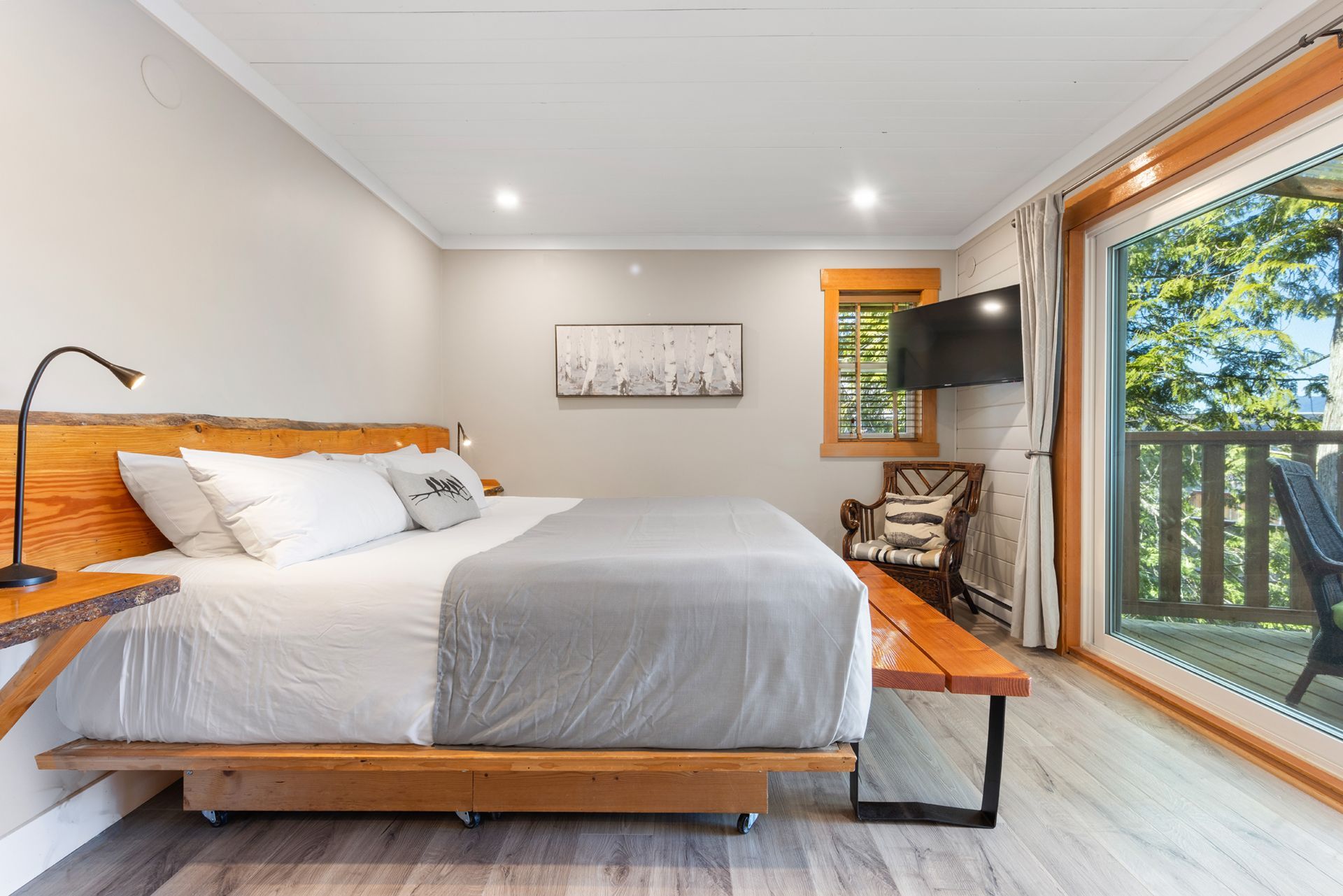 Moderne slaapkamer met een houten bed, wanddecoratie, tv, stoel en een glazen schuifdeur naar een balkon.